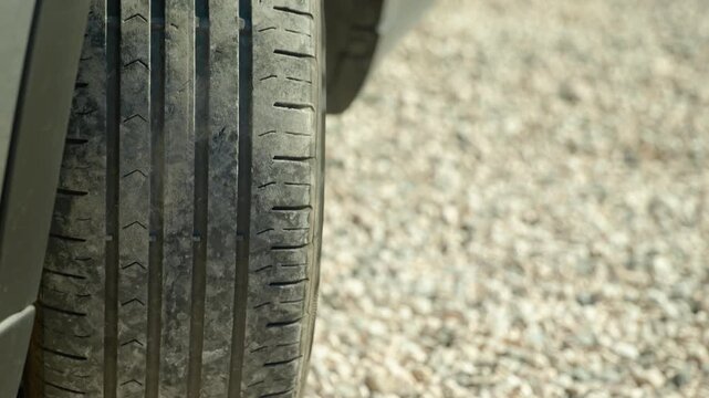 Car tire driving backward on a gravel road. Extreme close-up of a dirty car tire with visible tread pattern driving in reverse on a country gravel road, creating a motion blur effect on the ground