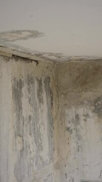 Water damage stains a ruined wall and ceiling corner inside a damaged house in close-up. The textured drywall decay highlights structural dampness for restoration and renovation media.