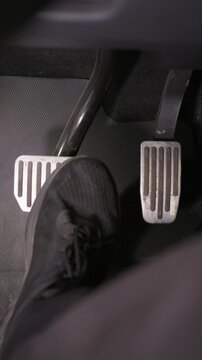 Person presses brake and accelerator pedals inside modern car cabin. Overhead perspective captures foot movement between metallic controls on textured rubber floor matting.
