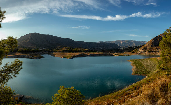 Panoramic view of Amadorio reservoir in Alicante with mountains and pine trees under blue sky
