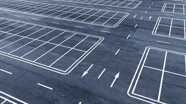 High angle view shows crisp white paint lines painted on fresh black asphalt inside an empty parking lot during daytime.