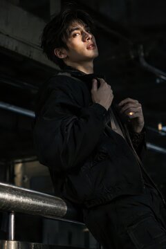 Young man in black jacket posing in dark urban industrial setting