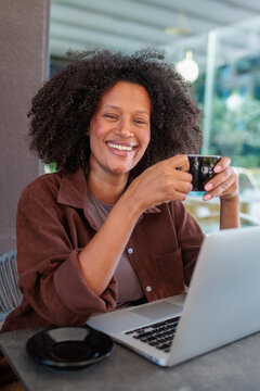 African woman sits at cafe table , smiling as she holds a coffee cup