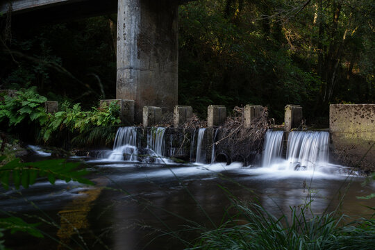 Long exposure of a small weir waterfall beneath a concrete bridge pier in the forest