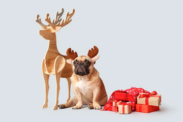 Cute French bulldog in reindeer horns with gift boxes and wooden deer on grey background. Christmas celebration © Pixel-Shot