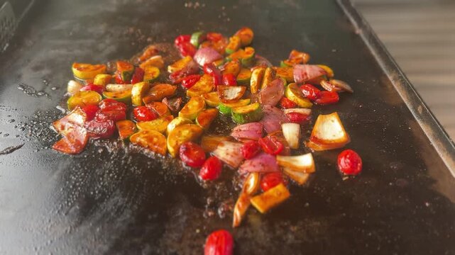 Sliced vegetables cook on a hot flat top griddle during food preparation