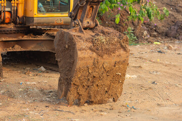 Front view of a large yellow excavator bucket coated with caked mud resting on dusty ground. © edy waluyo