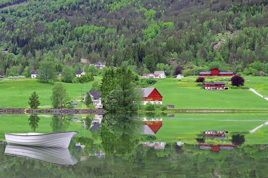 A white boat is reflected on a lake in a rural village, Stryn, Mindesundet, Fjordland, Norway