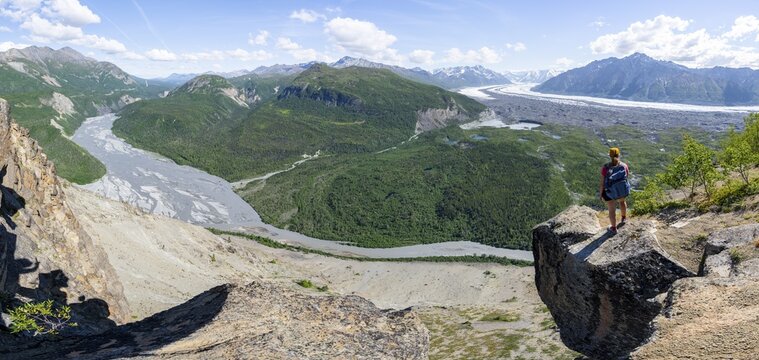 Panorama, young woman on a rocky outcrop enjoying the view, view of impressive mountain landscape with Matanuska glacier and glaciated mountain peaks, Matanuska River River, Lion's Head, Chugach Mountains, Alaska, USA