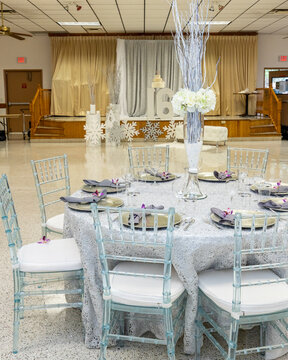 Silver sequin round table with branch centerpiece and clear chiavari chairs in a banquet hall