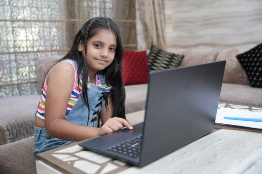 Cute little Indian girl child studying on laptop while sitting on sofa at home