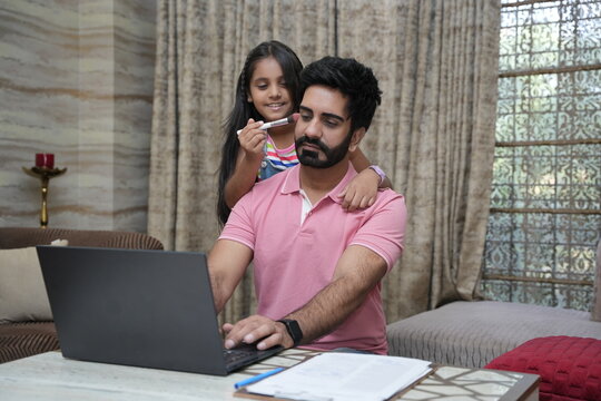 Indian father doing office work on laptop while her little daughter doing school home work. Concept of father and daughter working from home