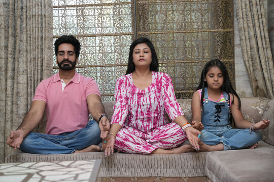 Indian happy family sits on the sofa and meditates at home