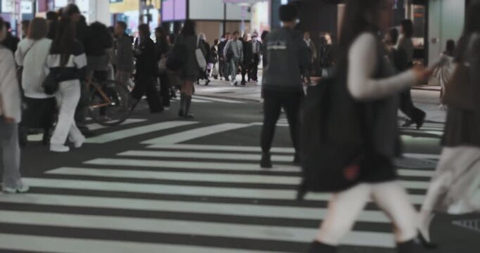 Many anonymous people cross pedestrian crossing in night city. Pedestrians crossing busy intersection on zebra crossing. Dynamic urban crosswalk. Pedestrian intersection in Japan metropolitan