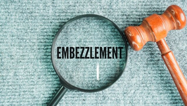 Judge's gavel and magnifying glass with the word Embezzlement is the crime of secretly taking or misusing money, property, or assets that have been entrusted to someone who has lawful access to them.