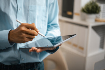 Tablet use by an adult holding a handheld tablet and touching its touchscreen with a stylus, bringing digital work into close view as the stylus contacts the display against a blurred background. © Garun Studios