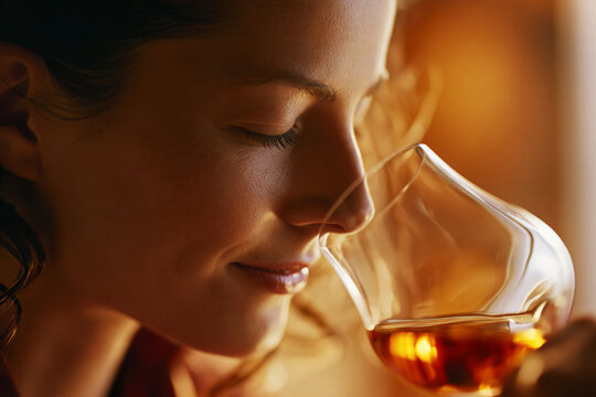 Young woman smelling a glass of amber colored whiskey with appreciation