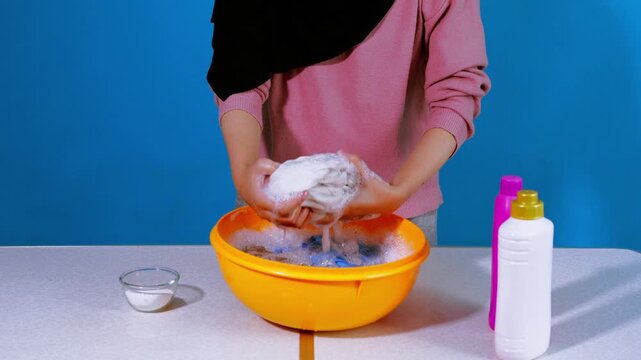 Person hand-washing and wringing out white garment in yellow basin of soapy water
