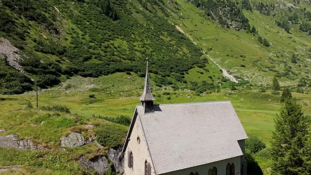 A small stone chapel with a pointed steeple stands amid lush Swiss hills