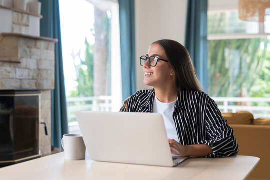 Woman writes a blog post on her laptop at home, pausing thoughtfully over content ideas in the living room. Blogging, online writing and content creation support an independent digital publishing.