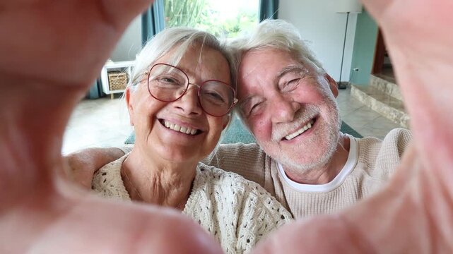 Happy senior couple smiling at the camera while making a heart shape with their hands. Cheerful old people enjoying retirement together at home, expressing love, care, and affection