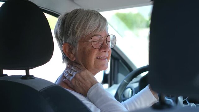 Senior woman rubs the side and back of her neck while seated behind the wheel. Her wince shows muscle pain, stiffness, driver fatigue, aging health concerns, and the need for road safety.
