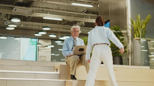 Young woman walks over and sits next to senior Thai man with laptop