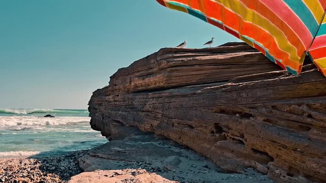 Point of view perspective of a beach scene with gulls on a cliff from under an umbrella