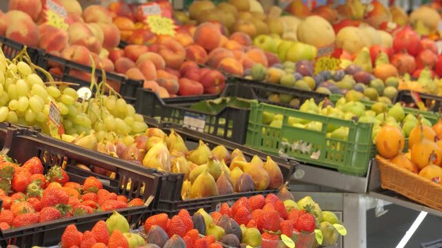The camera pans right across strawberries, grapes and figs in market crates, revealing peaches, apples and melons behind them.
