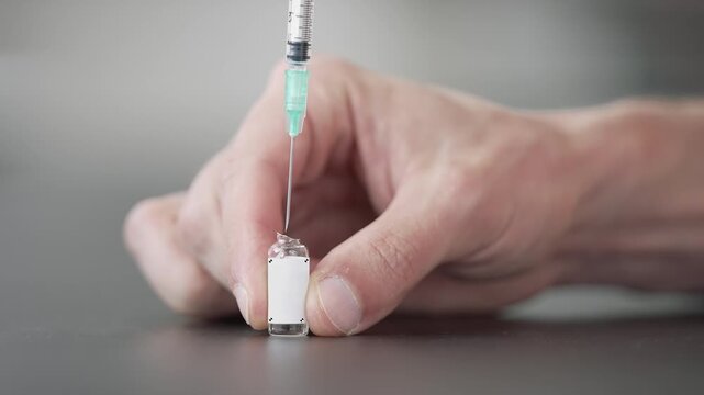 A blank ampoule with tracking markers stands on a table as a syringe needle goes in and starts drawing the liquid