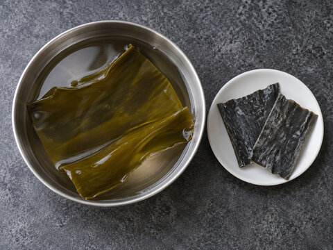 Dried kombu beside hydrated kelp soaking in a metal bowl