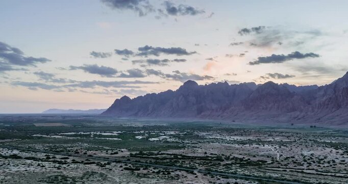 Aerial time-lapse of jagged Yinshan mountain ridge at dusk with pastel clouds over arid gobi grassland, Bayannur, Inner Mongolia, China
