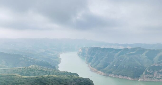 Aerial time-lapse of Yellow River winding through green gorge between loess hills under hazy sky, Laoniuwan, Pianguan county, Shanxi province, China
