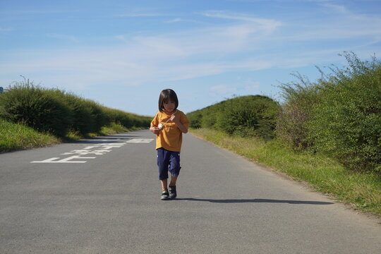 青空の下の一本道をカメラに向かってトコトコと歩いてくる小さな男の子