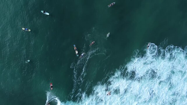 Overhead aerial landscape of tropical ocean lineup with surfers paddling and riding white foaming waves. Concept of outdoor adventure, ocean freedom, and active travel.