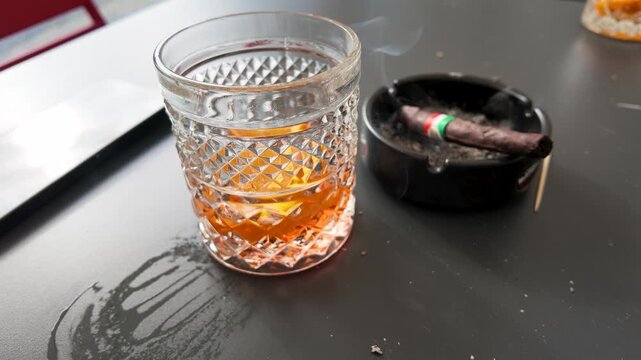 Glass of Amber Whiskey and Smoking Cigar in Ashtray on Table