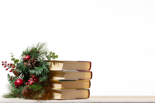 A stack of vintage books leaning against a Christmas wreath with pinecones. Ideal for literary holiday greeting cards, seasonal library events, and heartwarming winter education marketing.