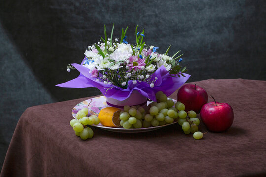 bouquet of flowers, a lemon, grapes, and apples on a table