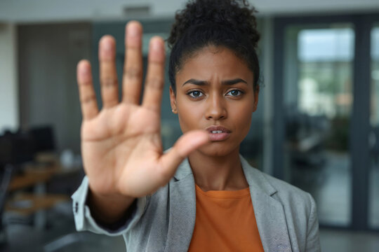 Young black woman stops with a firm hand gesture. No to violence in the office workplace. Her expression conveys clear refusal or warning