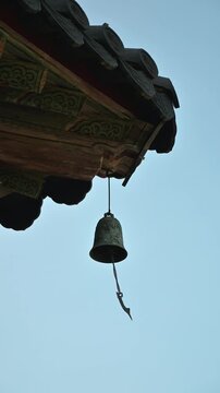 푸른 하늘을 배경으로 법주사 팔상전 목조 처마 밑에서 흔들리는 물고기 풍경.(Wind chime with fish pendant swaying under Beopjusa Palsangjeon wooden eaves against blue sky.)