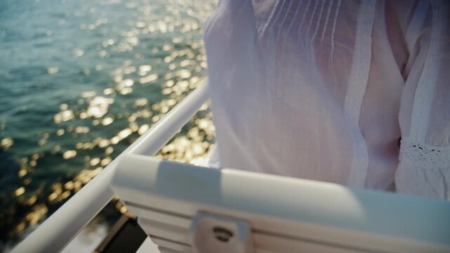 Close-up of an older woman's white pintucked blouse at a ferry rail above sun-glittering sea and boat wake, French Riviera, France.
