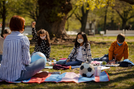Children raising hands during outdoor lesson on blanket