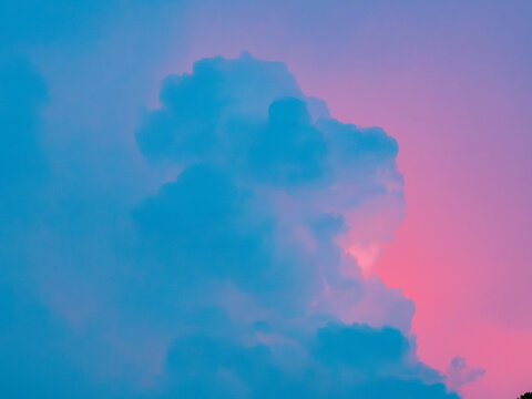 Blue cumulus cloud against a vivid pink and purple sunset sky, dreamy surreal pastel gradient cloudscape with soft glowing light