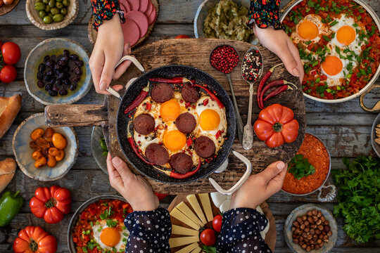 Fried eggs with turkish sausage named sucuk. Sucuklu yumurta. Hands of two women sharing and holding their meal.  