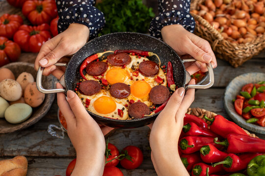 Fried eggs with turkish sausage named sucuk. Sucuklu yumurta. Hands of two women sharing and holding their meal.  