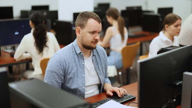 Side view on concentrated male student sitting at library desk with pc, preparing for exam in computer class . High quality 4k footage