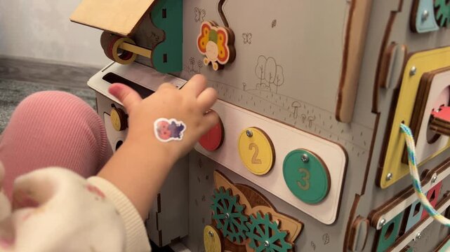 A child touches numbered circles and turns a butterfly piece on a busy board, early numeracy, sensory learning, motor skills.