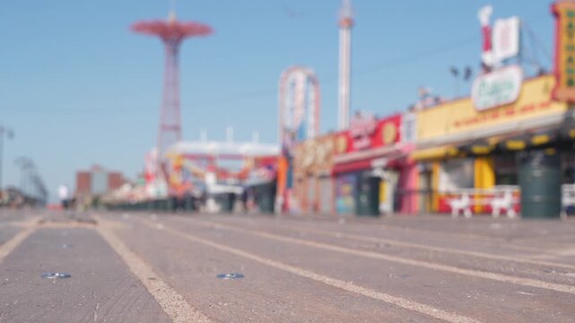 Coney Island beach promenade in Brooklyn, New York, United States. Wooden boardwalk near retro luna park. Amusement park on ocean coast beach. Waterfront summer holiday, people walking on promenade.