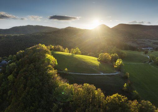 Drone view of  small mountain village in Slovakia surrounded by forests, and rolling hills in vibrant fall colors, bathed in golden afternoon light.