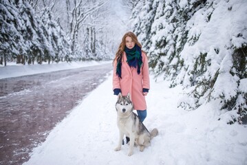 Red-haired girl standing with a husky dog near a snowy forest road © Nomad_Soul